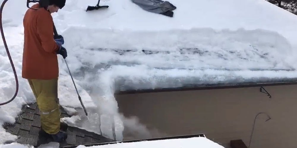 A professional steaming an ice dam off a roof