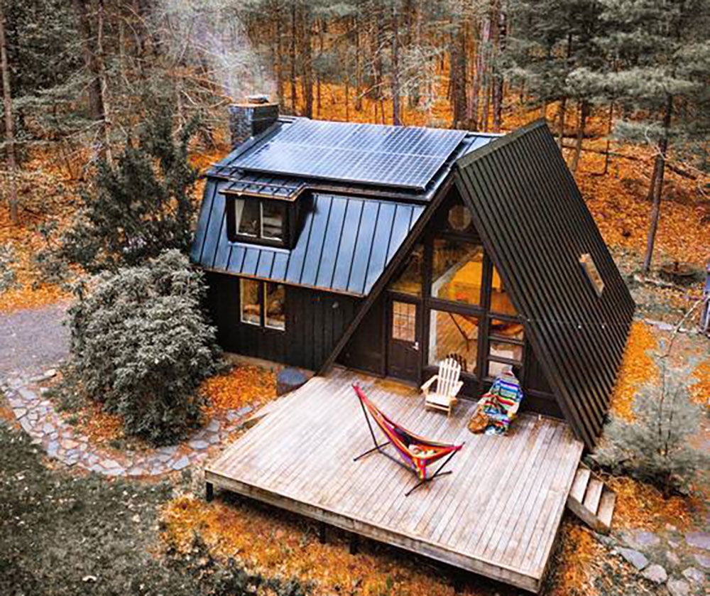 A charming A-frame cabin with rooftop solar panels, surrounded by pine trees. 