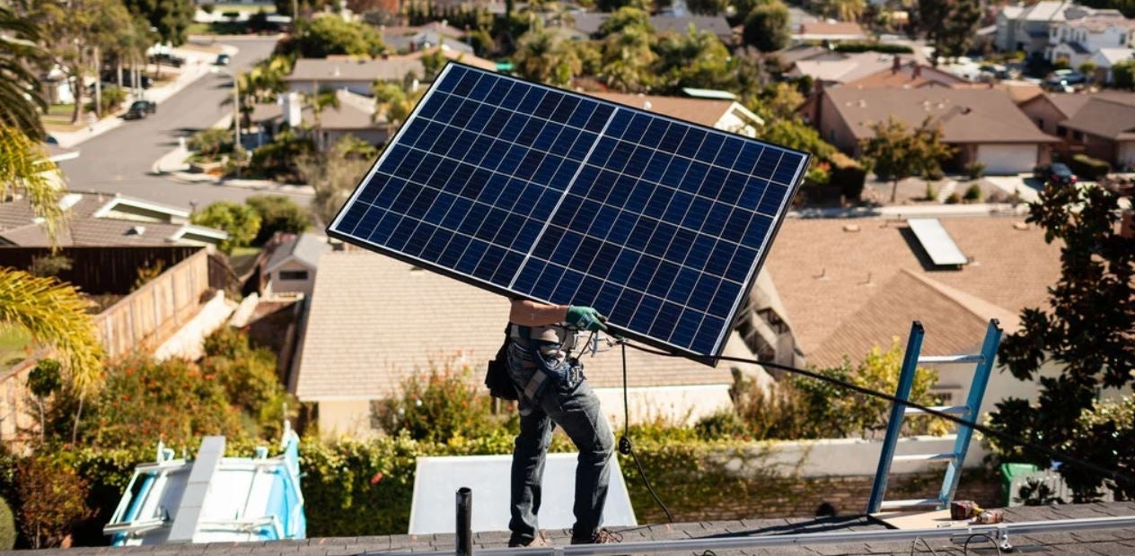 Installer carries solar panel on roof