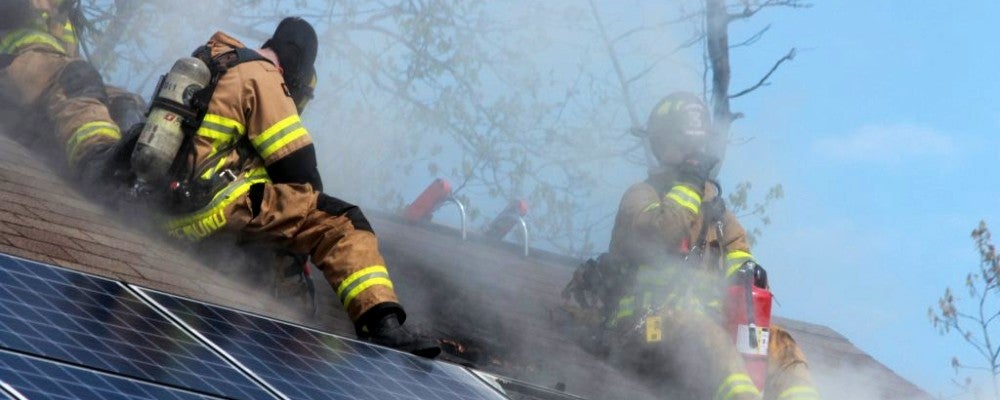 Firefighters on smoldering roof with solar panels