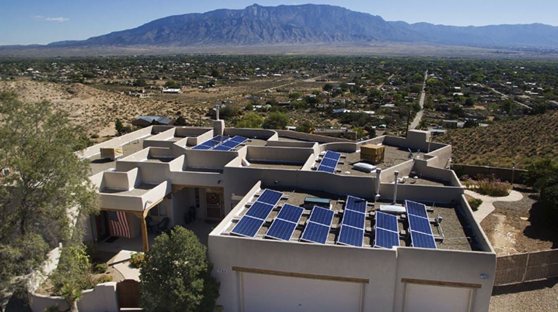 Aerial shot of a home with rooftop solar panels, with arid New Mexico landscape in the background