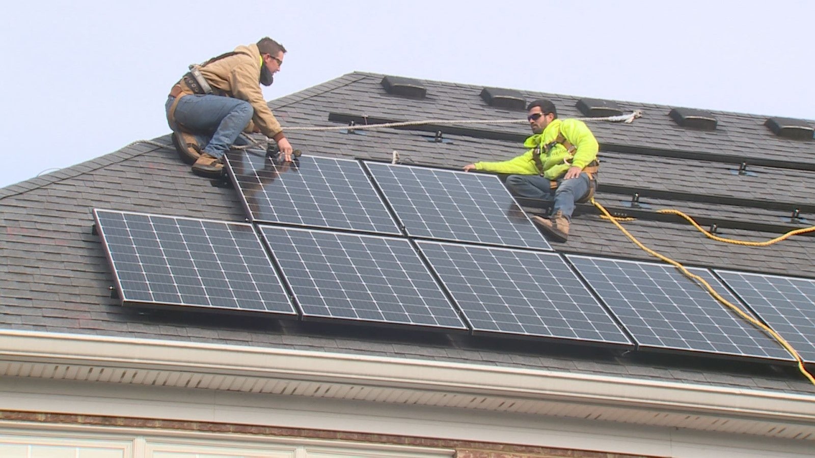 two tradesmen install solar panels on a shingled rooftop