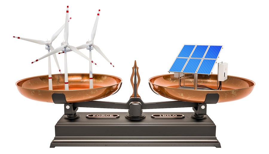 Wind turbines being weighed against solar panels on a scale