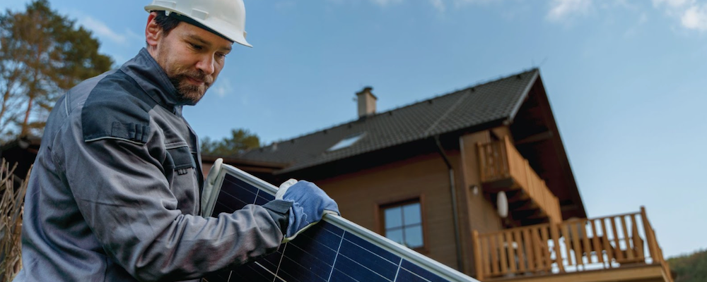 Solar panel installer holding a solar panel in front of a home
