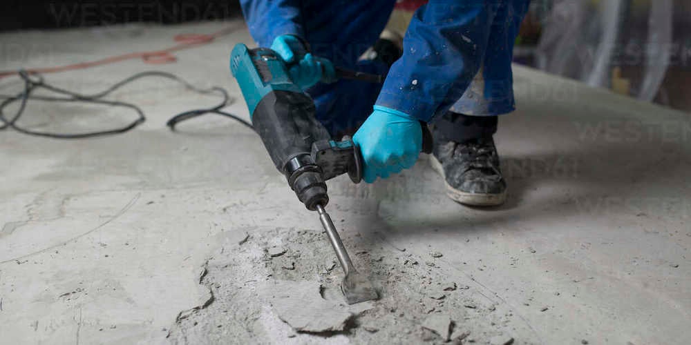A professional jackhammering concrete in a basement