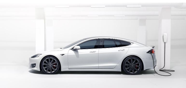 A Tesla Model S connected to a Wall Connector in a white room